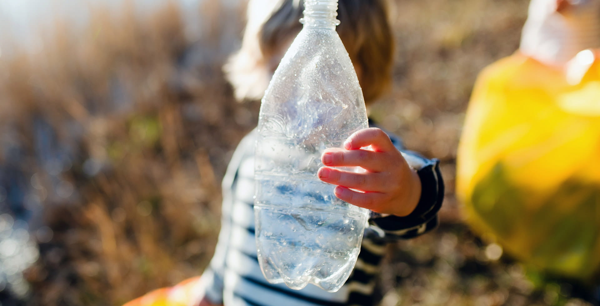 Un bambino tiene in mano una bottiglia in plastica contro sole – Il potenziale degli imballaggi sostenibili